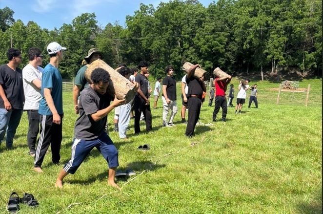 Campers carrying logs on their shoulders in a field